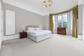 A bedroom with a large bed, bedside tables, a dresser, and a window with curtains. - Three Bedroom Hampstead Apartment (London)