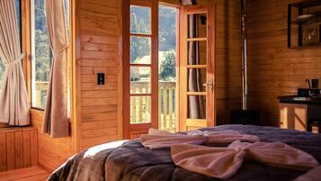 Una habitación de madera con una cama, un ventanal y una puerta que da al exterior.