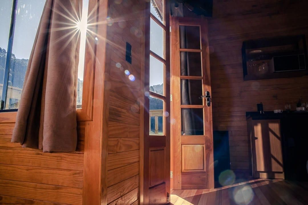 Un interior de madera con una puerta que da a un balcón, una ventana con cortinas y una zona de cocina.