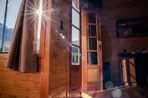 Ein Holzinnenraum mit einer zur Balkon führenden Tür, einem Fenster mit Vorhängen und einer Küchenzeile.