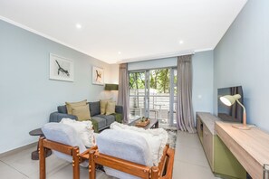 Ein modernes Wohnzimmer mit einer Couch, zwei Sesseln, einem Couchtisch, einem Fernseher und einem Schreibtisch mit einer Lampe.