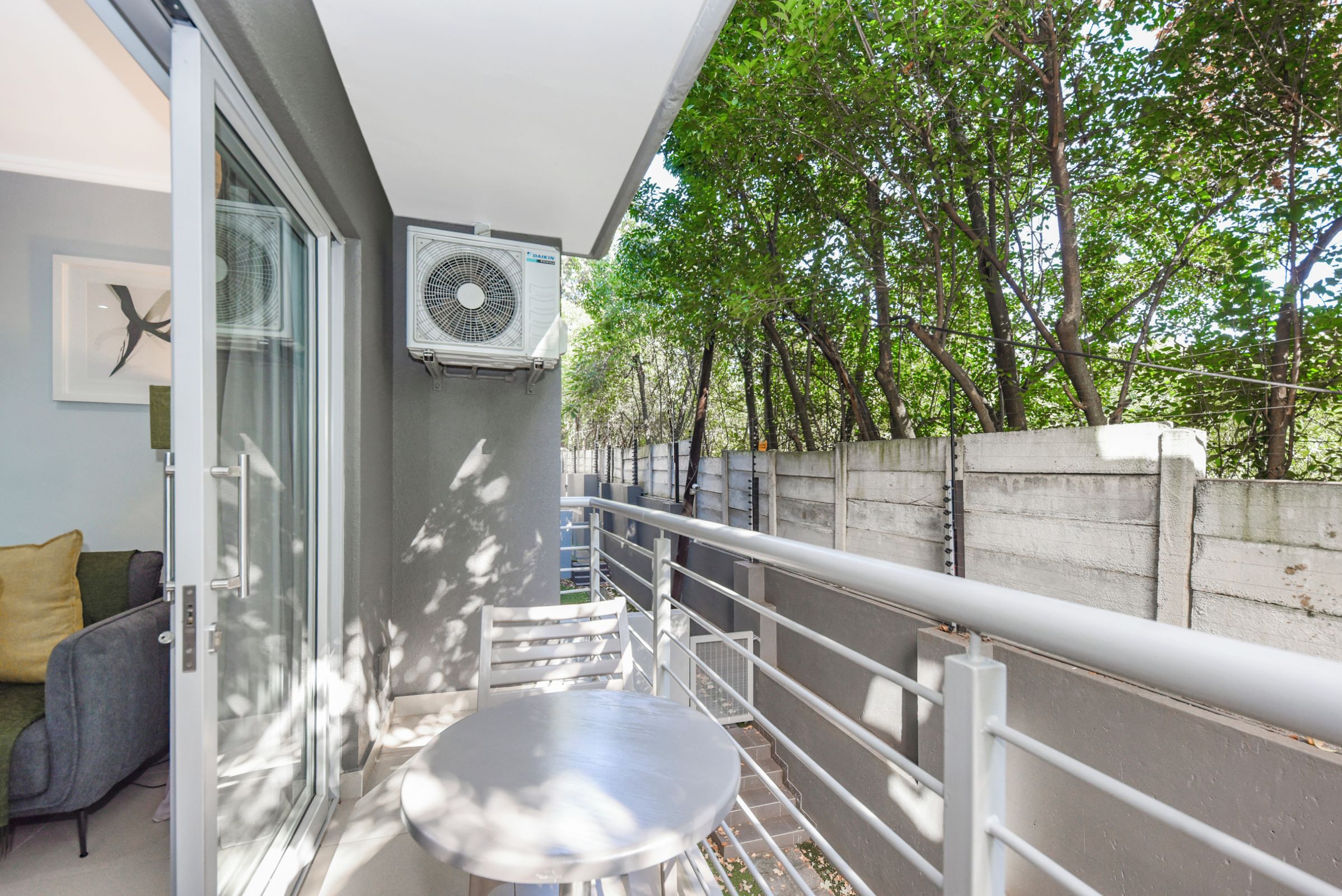 Un balcon avec une table et des chaises, une porte vitrée et un climatiseur fixé au mur.