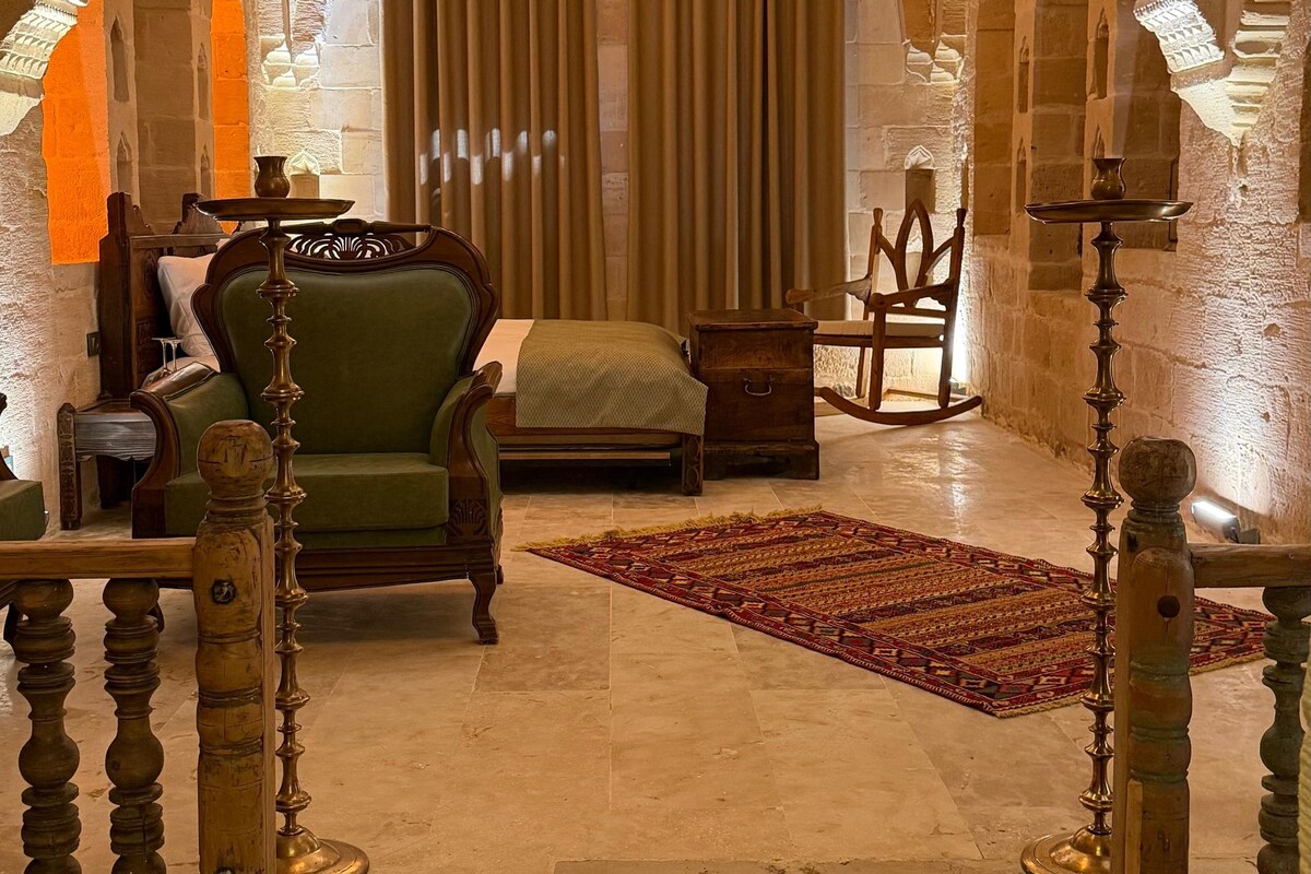 Una habitación con techo abovedado de piedra, un sofá verde, una silla de madera, una mesita pequeña y una alfombra estampada.