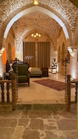 A room with a stone arch ceiling, a green sofa, a wooden chair, a small table, and a patterned rug.