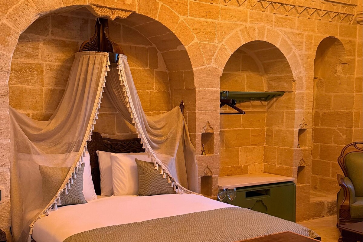Una cama con dosel, un aparador de madera y una pared de piedra con nichos abovedados.