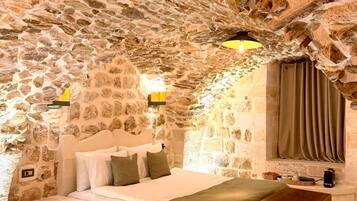 Un dormitorio con paredes de piedra, una cama, una lámpara de noche y un cofre de madera.