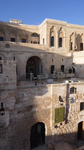 A courtyard with stone architecture, outdoor seating, and a flag. - YONA OTEL (ARTUKLU)