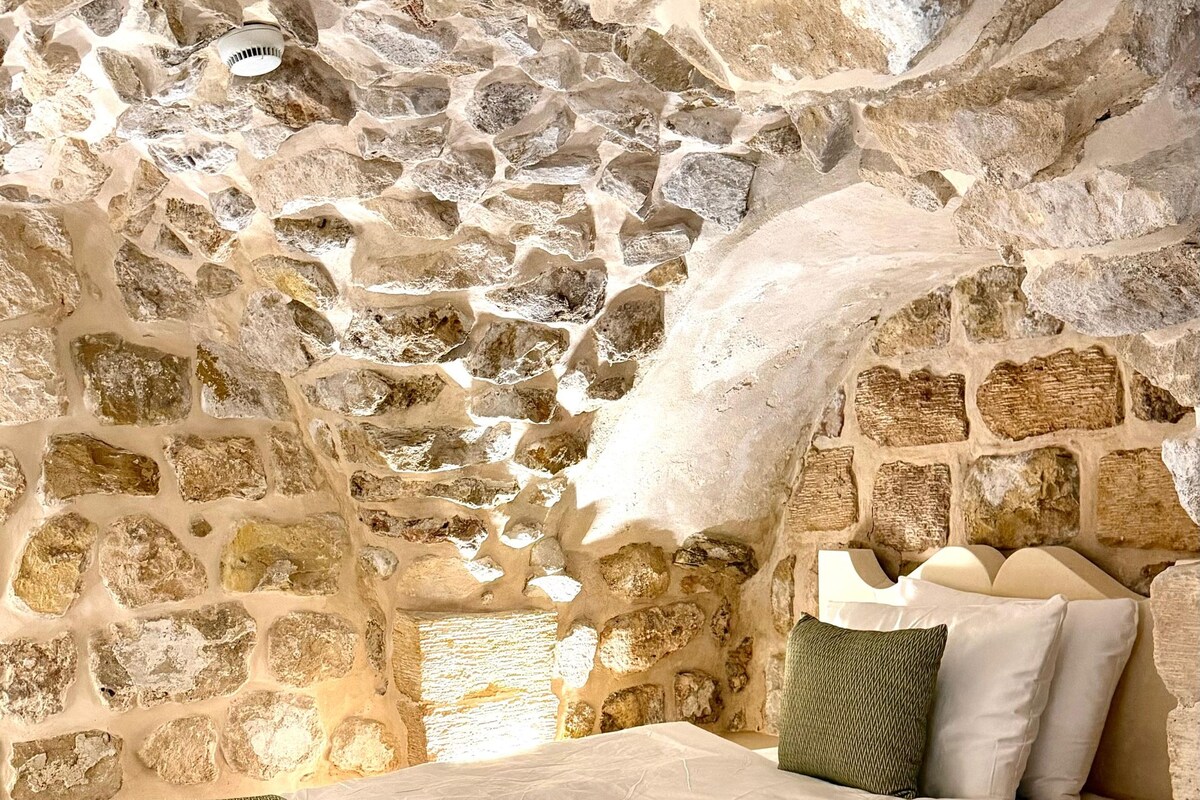 Una habitación de paredes de piedra con una cama, almohadas y una manta estampada.