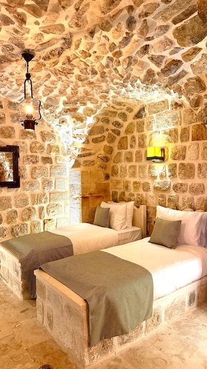 Habitación de paredes de piedra con dos camas, una lámpara colgante y una lámpara de pared.