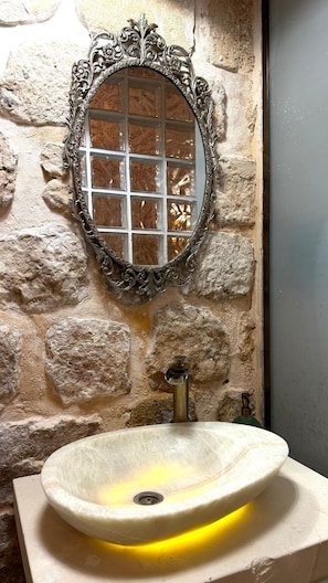 Un baño con pared de piedra, un espejo decorativo y un lavabo sobre encimera.
