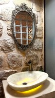 Un baño con pared de piedra, un espejo decorativo y un lavabo sobre encimera.