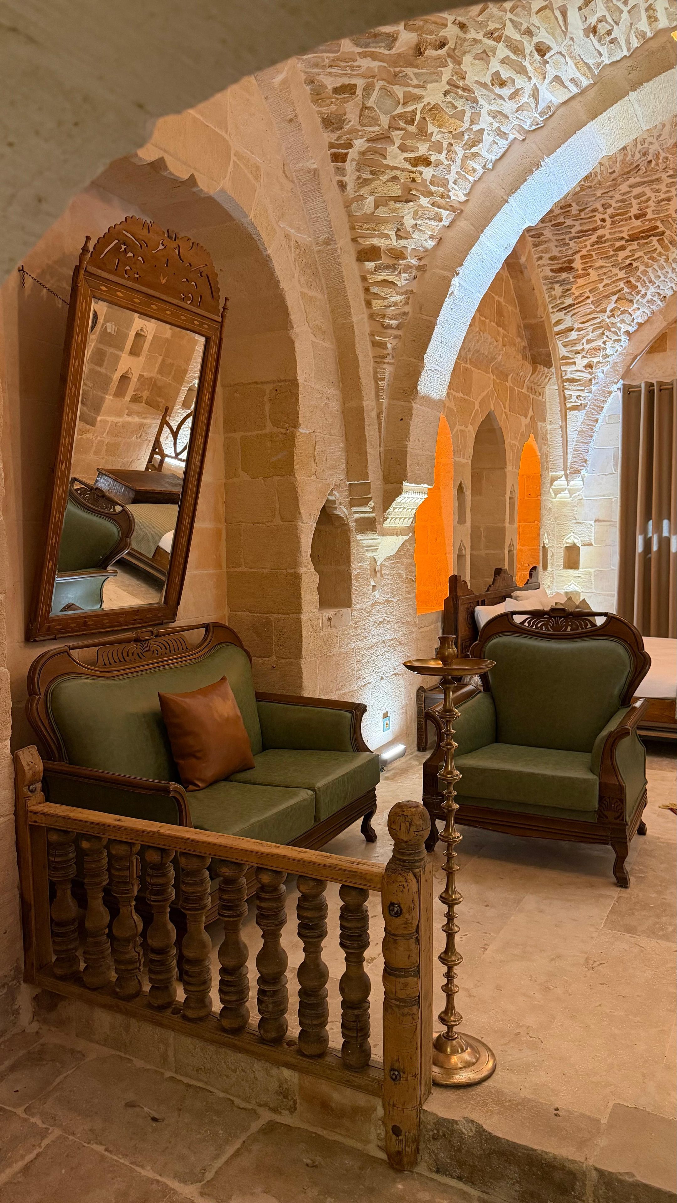 Una habitación con paredes de piedra, un banco de madera, un sofá verde y un espejo.
