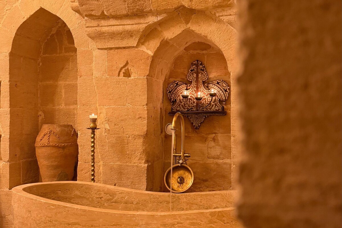 Una habitación con paredes de piedra, un lavabo grande, una olla pequeña y un accesorio fijado a la pared.