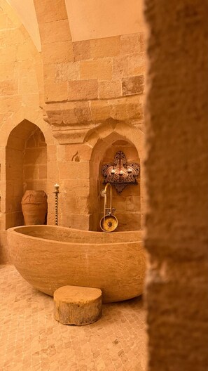 A stone-walled room with a large basin, a small pot, and a wall-mounted fixture. - YONA OTEL (ARTUKLU)