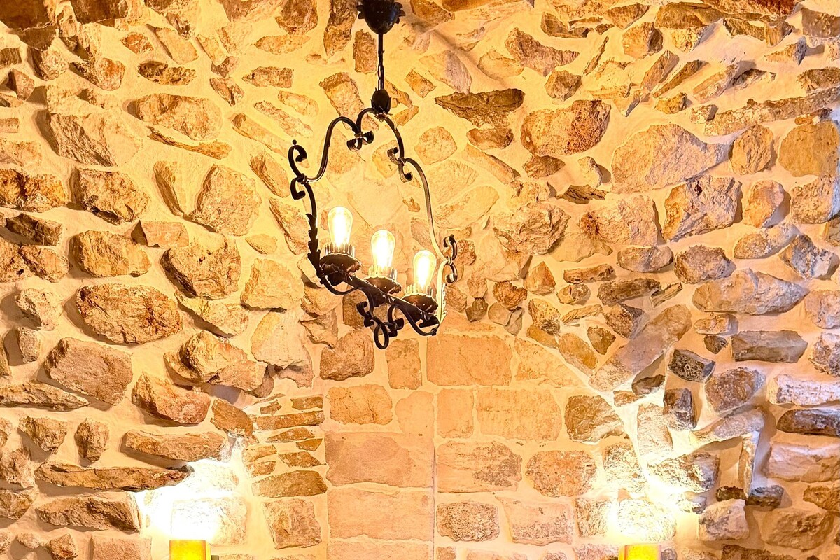 Un dormitorio con pared de piedra, una cama con cabecera de madera, dos lámparas de noche y una alfombra estampada.