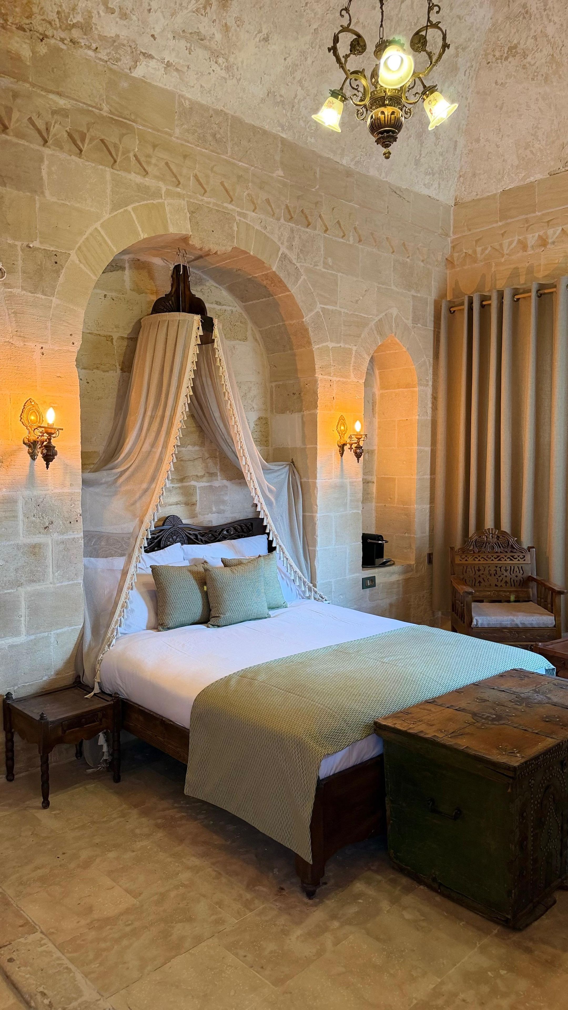 A room with a four-poster bed, stone walls, and a chandelier.