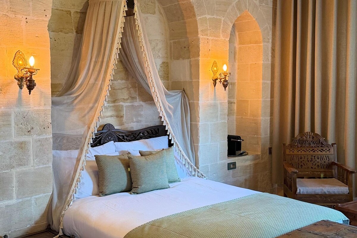 Una habitación con cama con dosel, paredes de piedra y una araña.
