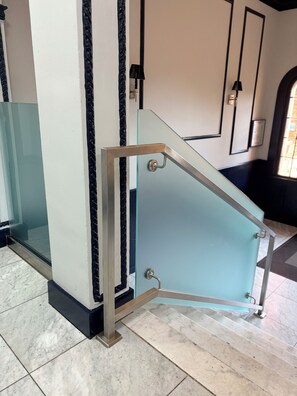 Un intérieur moderne avec un escalier à garde-corps en verre, un sol en marbre et un mur orné d’œuvres d’art encadrées.