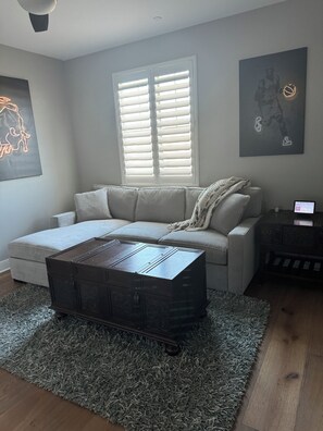 A living room with a sofa, a coffee table, a rug, a window with blinds, and artwork on the walls. - Cozy 1-bedroom apartment in perfect Winchester with AC (Winchester)