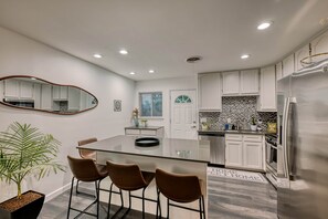 A modern kitchen with a central island, bar stools, a dining table, and a large mirror. - Remodeled 2BR | Near Mueller, UT & Downtown (Austin)