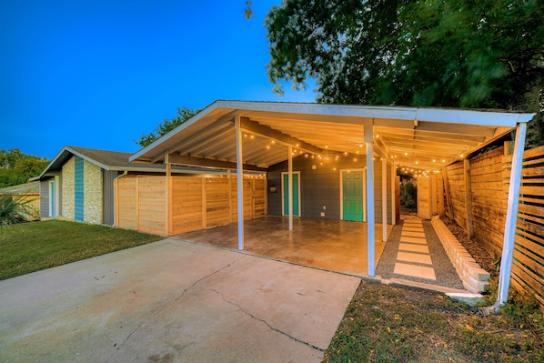 A covered garage with a concrete driveway, wooden garage doors, and string lights. - Remodeled 2BR | Near Mueller, UT & Downtown (Austin)