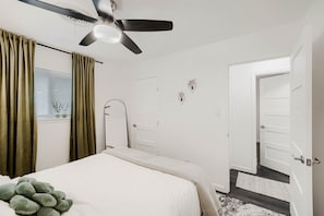A bedroom with a bed, a ceiling fan, a window with curtains, and a door. - Remodeled 2BR | Near Mueller, UT & Downtown (Austin)