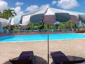 Ein Swimmingpool mit Liegestühlen und Sonnenschirmen, umgeben von einem Zaun und Palmen.