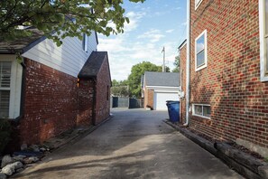 A narrow alleyway between two brick buildings with a garage door visible in the distance. - Luxury Warm Modern Retreat in Utica Square w/ 2 King Suites, 3 Patios & Spa Bath (Tulsa)