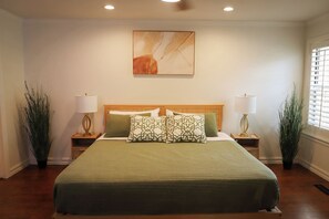 A bedroom with a large bed, two bedside tables, a wall-mounted painting, and two floor lamps. - Luxury Warm Modern Retreat in Utica Square w/ 2 King Suites, 3 Patios & Spa Bath (Tulsa)