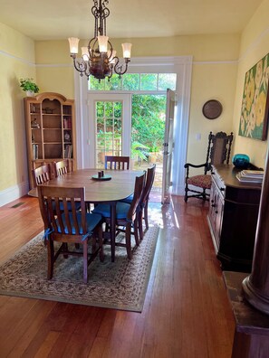 A dining room with a wooden table, chairs, a chandelier, a bookshelf, and a view through a glass door to a garden. - Easy SF Access from Spacious apartment in Sausalito with stunning views (Sausalito)