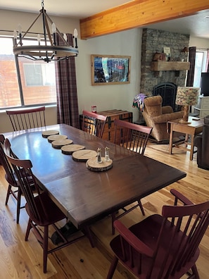Un comedor con una larga mesa de madera, sillas, una araña y una chimenea de piedra.