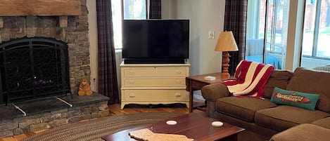 Una sala de estar con chimenea de piedra, un televisor de pantalla plana, un sofá, una mesa de centro y un tapete estampado.