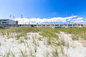 A beachfront hotel with multiple-story buildings, a sandy foreground with grass, and a clear blue sky. - 55 S Atlantic Ave 4-20 (Cocoa Beach)