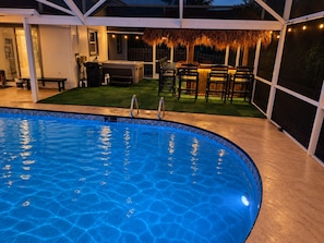 A swimming pool with a tiled edge, surrounded by a deck area with outdoor seating and a thatched roof structure. - 122 Sunset Dr (Cocoa Beach)