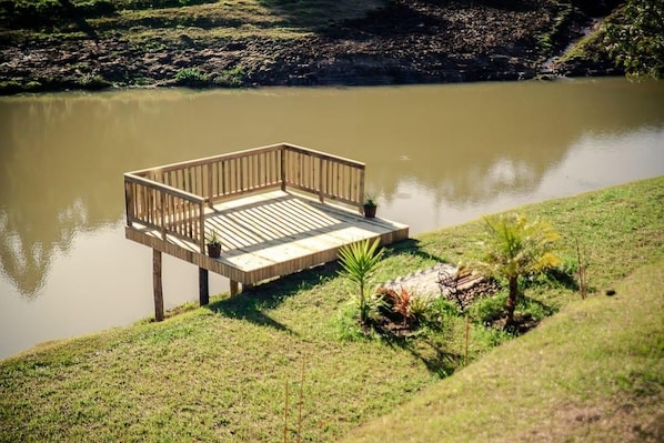 A wooden deck extending over a calm body of water, surrounded by grassy banks and small plants. - Blue Sunset 4 (Urubici)
