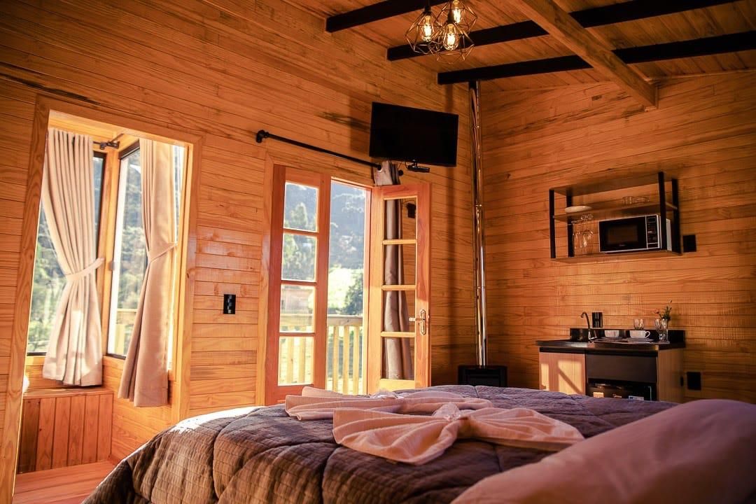 A wooden cabin bedroom with a bed, a television, a microwave, and a window with curtains.