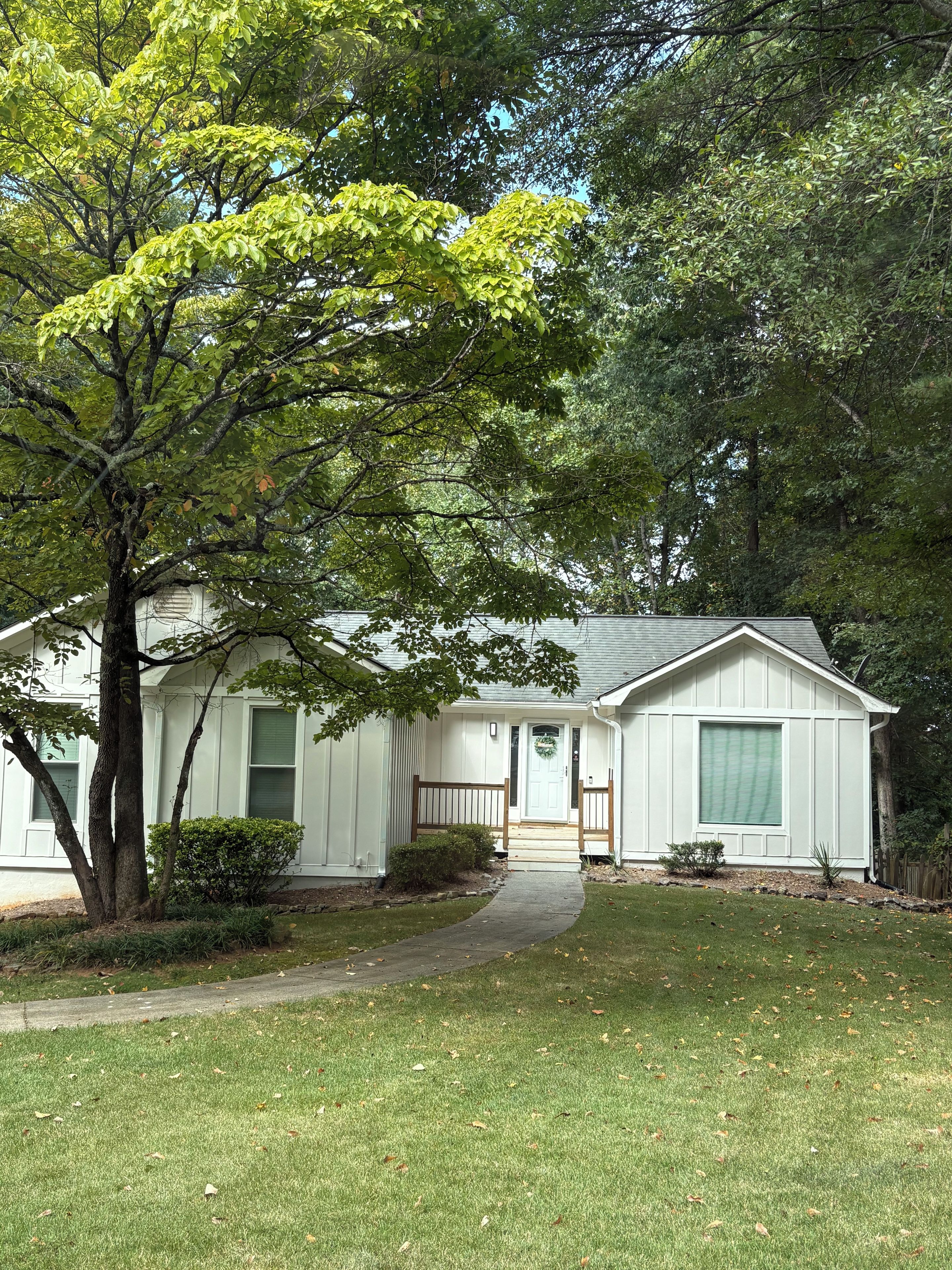 A single-story house with a front porch, a small front yard, and a tree in the foreground.