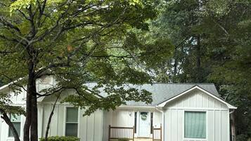 A single-story house with a front porch, a small front yard, and a tree in the foreground.