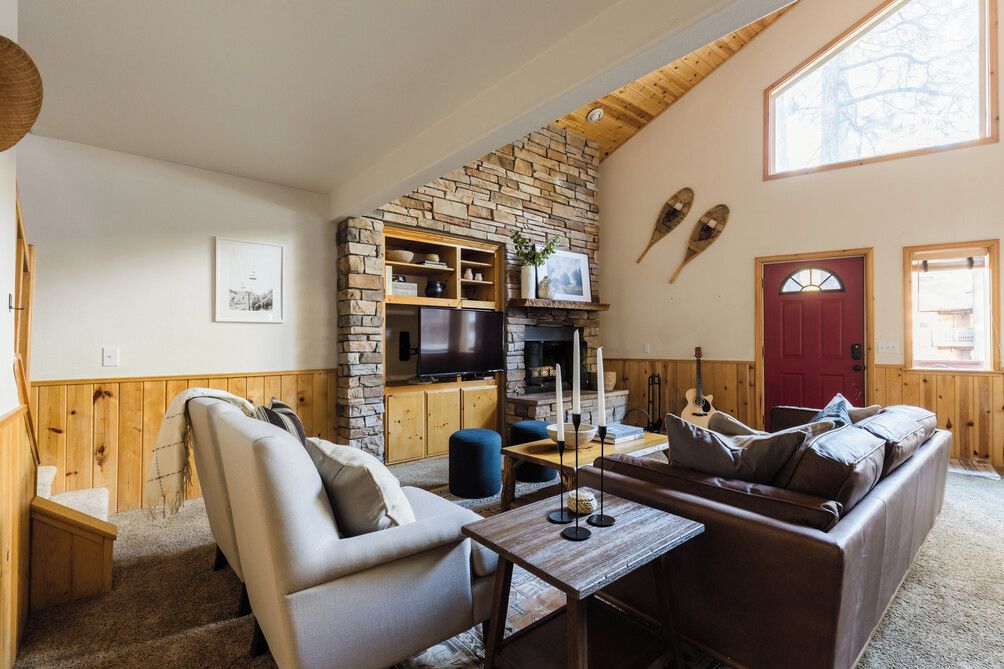 A cozy living room with a stone fireplace, a television, and a red door.
