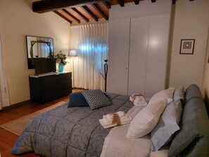 Ein Schlafzimmer mit einem Bett, einem Schminktisch, einem Spiegel, einer Lampe und einem Fenster mit Vorhängen.