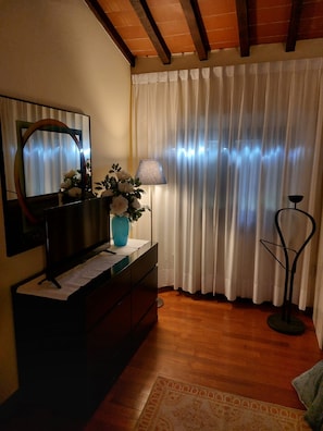 Ein Zimmer mit Holzboden, einem Schminktisch mit Spiegel, einer Vase mit Blumen, einer Lampe und einem Vorhang.