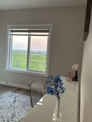 Una habitación con un amplio ventanal, vista despejada a un paisaje verde, una mesa blanca con un jarrón de flores y una silla.