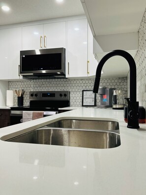A modern kitchen with stainless steel appliances, a large sink, and a microwave above the stove. - Sheen’s Suite-Walkout Basement with Scenic Views (Calgary)