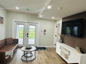 A modern living room with a brown leather sofa, a round coffee table, and a flat-screen TV mounted on a wooden panel wall. - Sheen’s Suite-Walkout Basement with Scenic Views (Calgary)