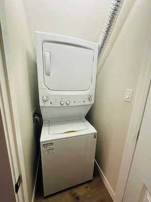 A compact washer and dryer unit in a narrow laundry room with a sloped ceiling and a vent. - Sheen’s Suite-Walkout Basement with Scenic Views (Calgary)