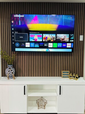 A flat-screen TV mounted on a wall with a wooden panel backdrop, displaying a streaming service interface with various content options. - Sheen’s Suite-Walkout Basement with Scenic Views (Calgary)