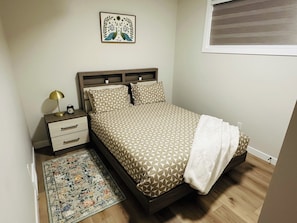 A bedroom with a bed, nightstand, lamp, and a decorative wall piece. - Sheen’s Suite-Walkout Basement with Scenic Views (Calgary)