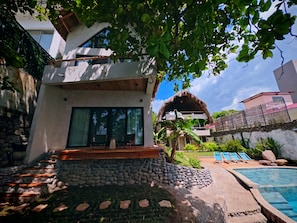 Ein modernes Haus mit einer Steintreppe, die zu einer Holzterrasse, einem Pool und einem Gebäude mit Strohdach führt.