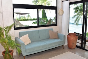 Ein Zimmer mit einem hellblauen Sofa, einer Topfpflanze, einem großen Fenster mit Meerblick und einem rustikalen Tonkrug.