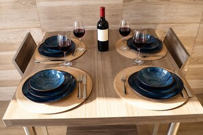 A dining table set with blue plates, silverware, and wine glasses, with a bottle of red wine in the center. - New Listing (Roma)